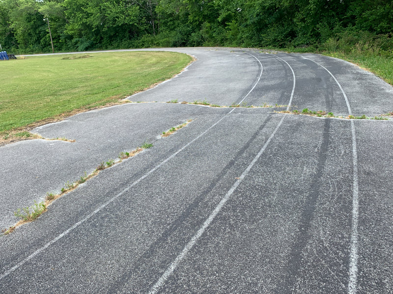 The old asphalt track curving past a grassy field before restoration