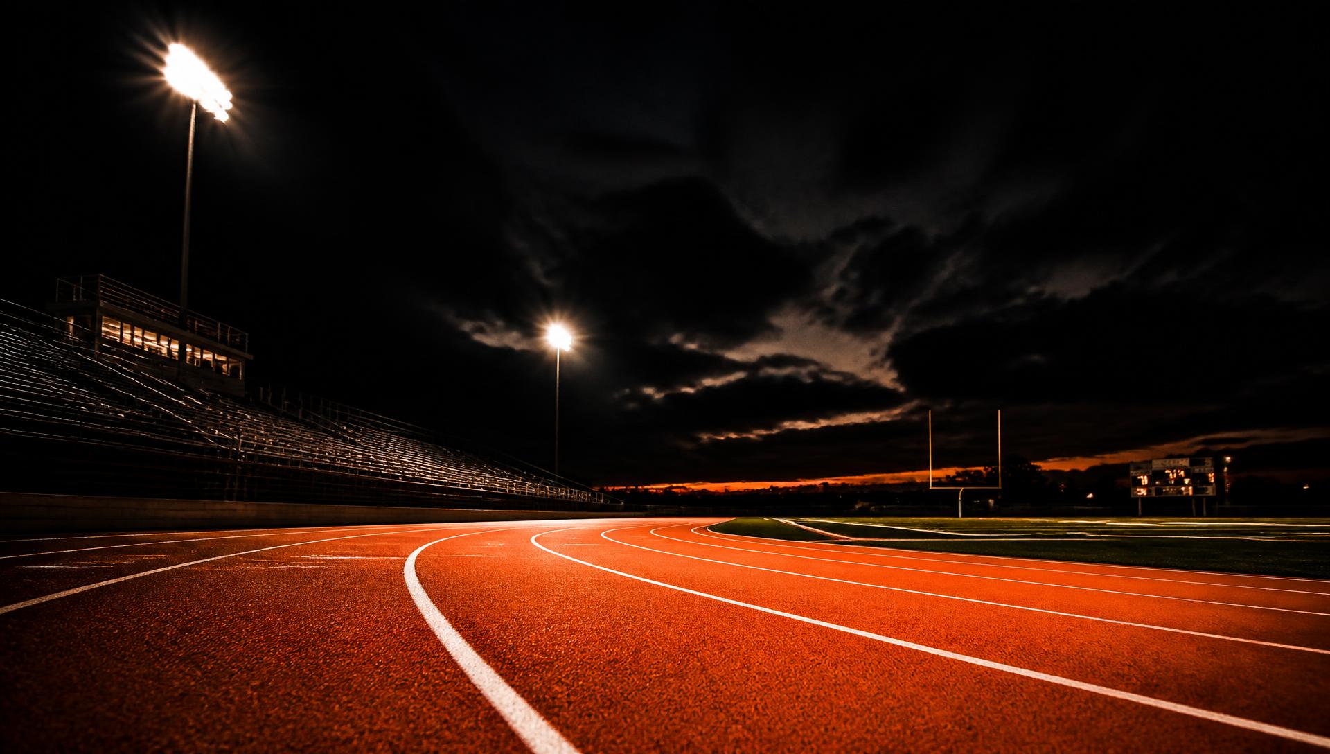 Empty running track lit by stadium lights at dusk